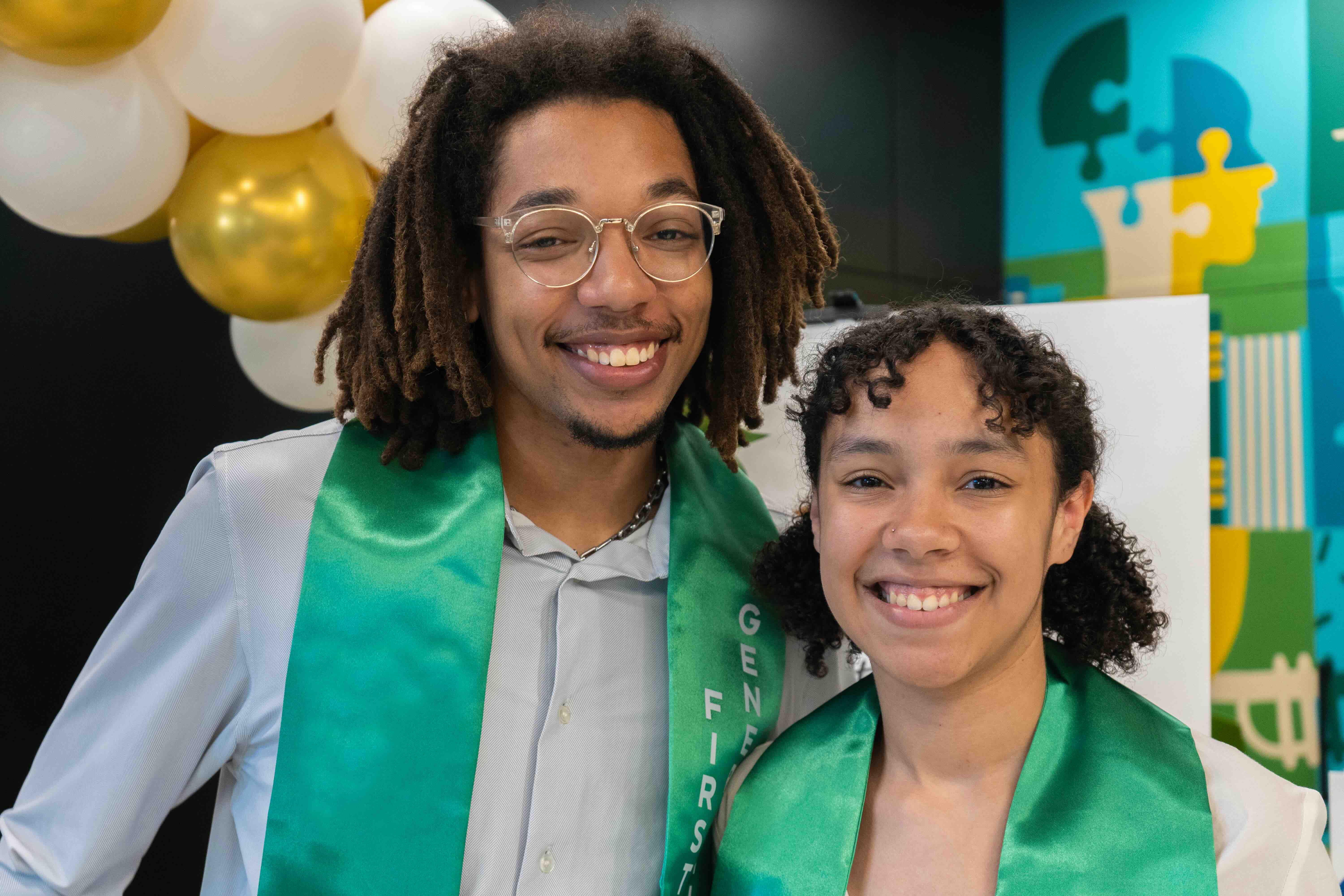 Two smiling young people in green sashes, celebrating.