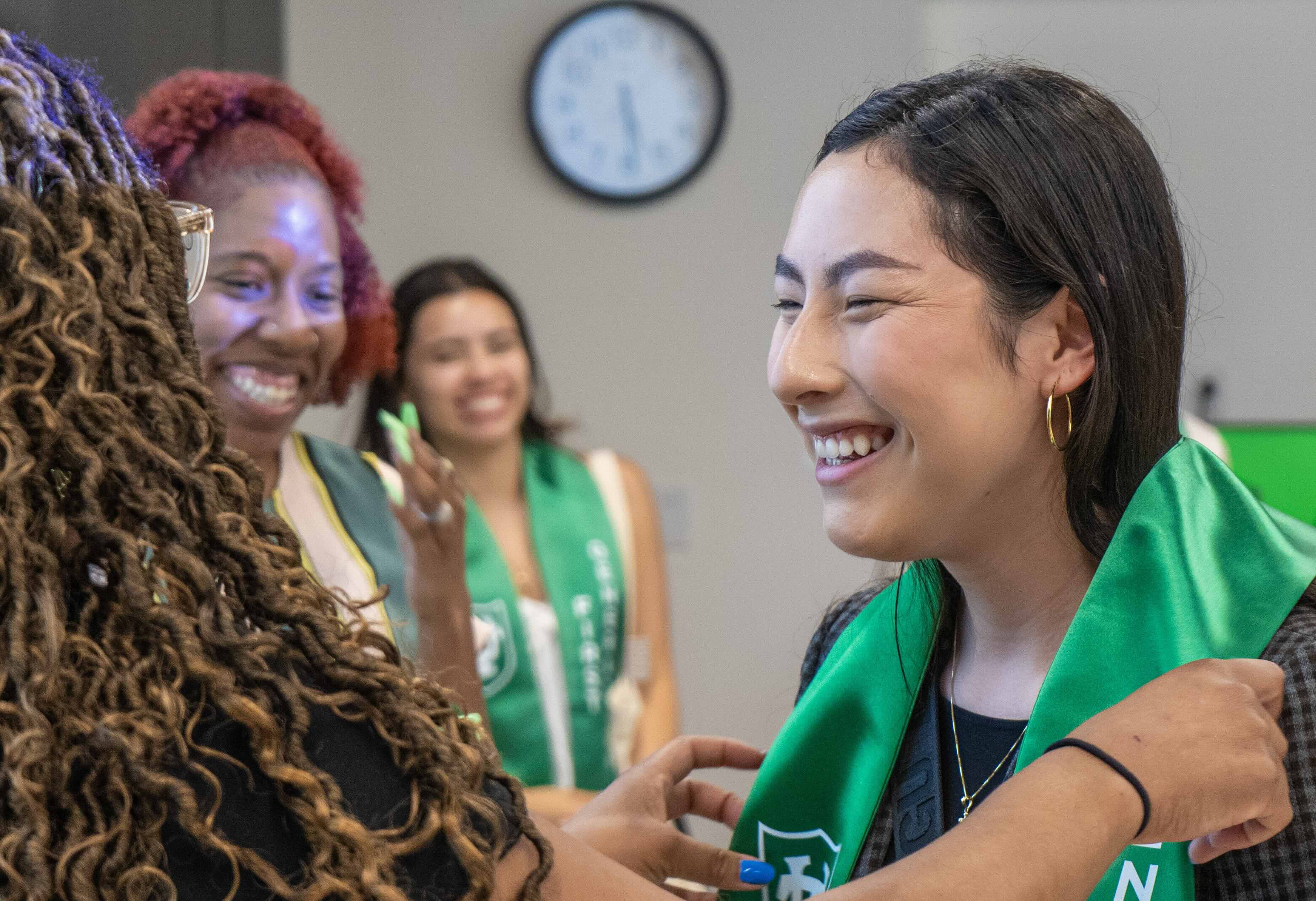 Smiling woman receives green graduation stole as others watch.
