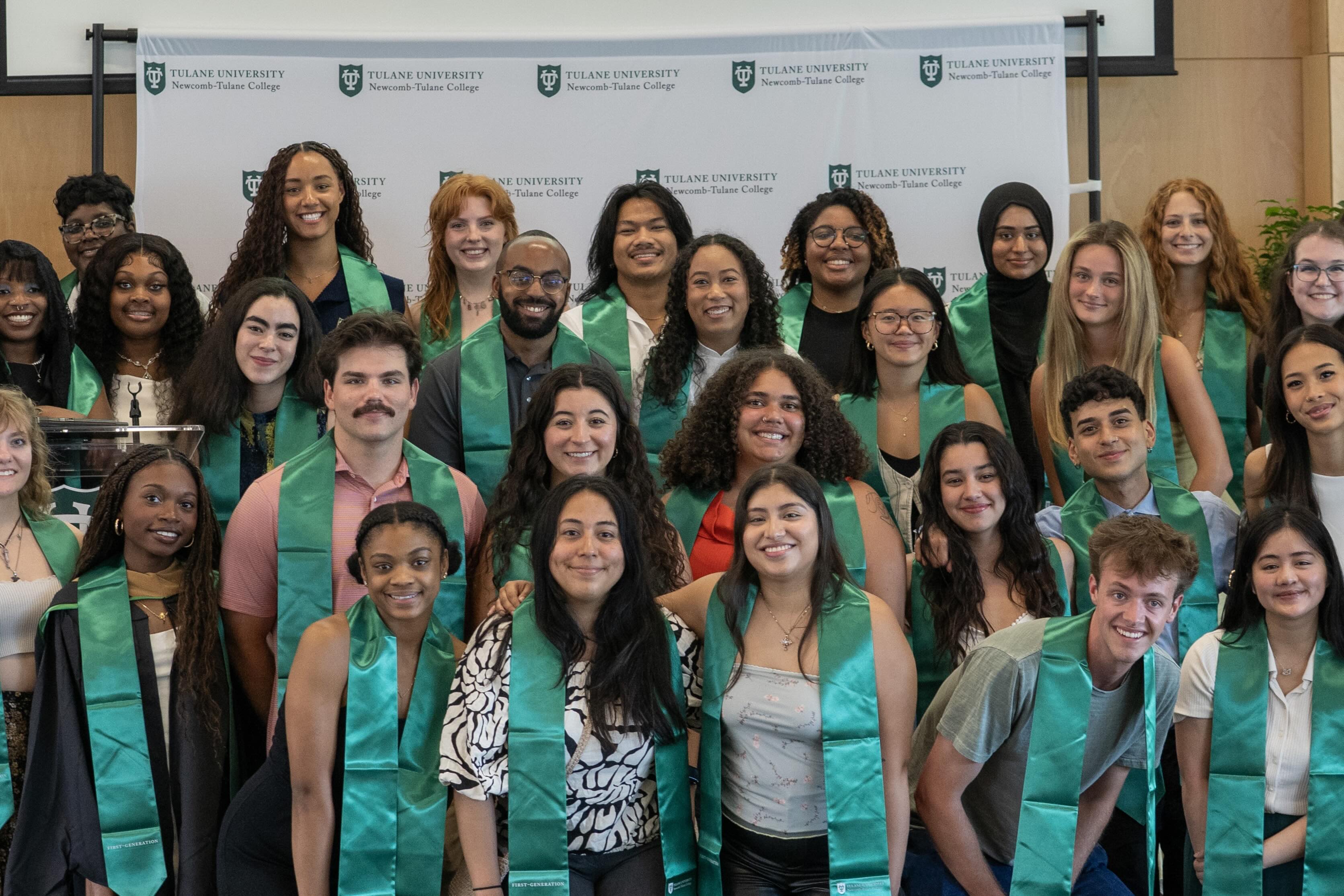 Happy students in green sashes and gowns pose for a group photo.