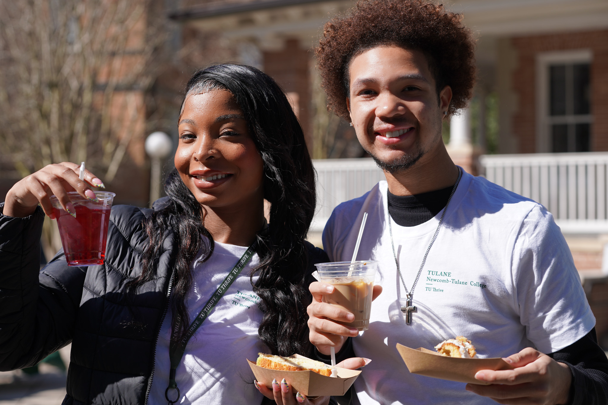Smiling woman and man hold drinks and snacks, enjoying an outdoor event.