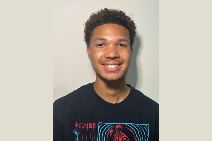 Smiling young man with curly hair wearing a dark shirt.