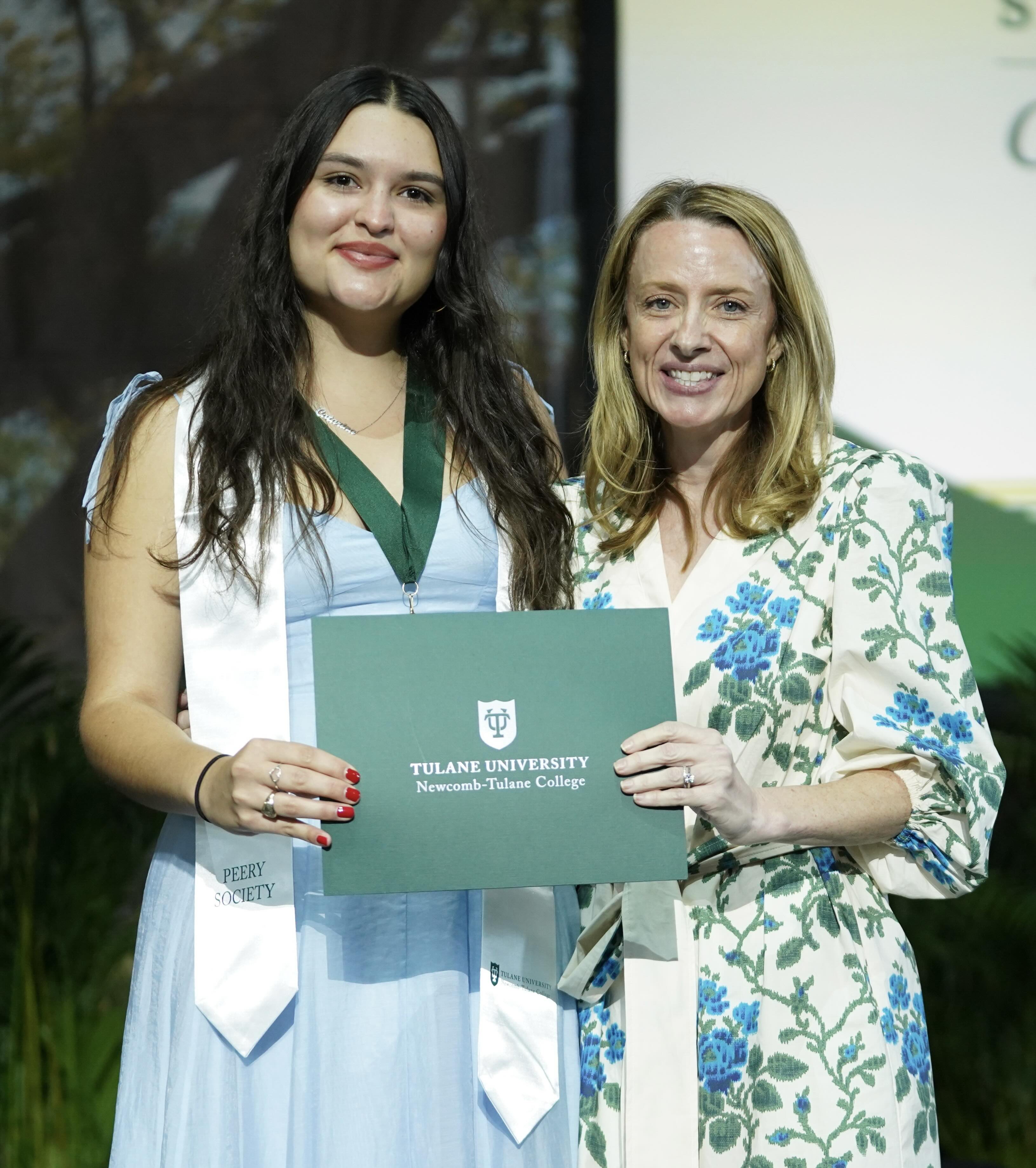 Graduate in blue dress and woman in floral dress smile, holding a Tulane certificate.
