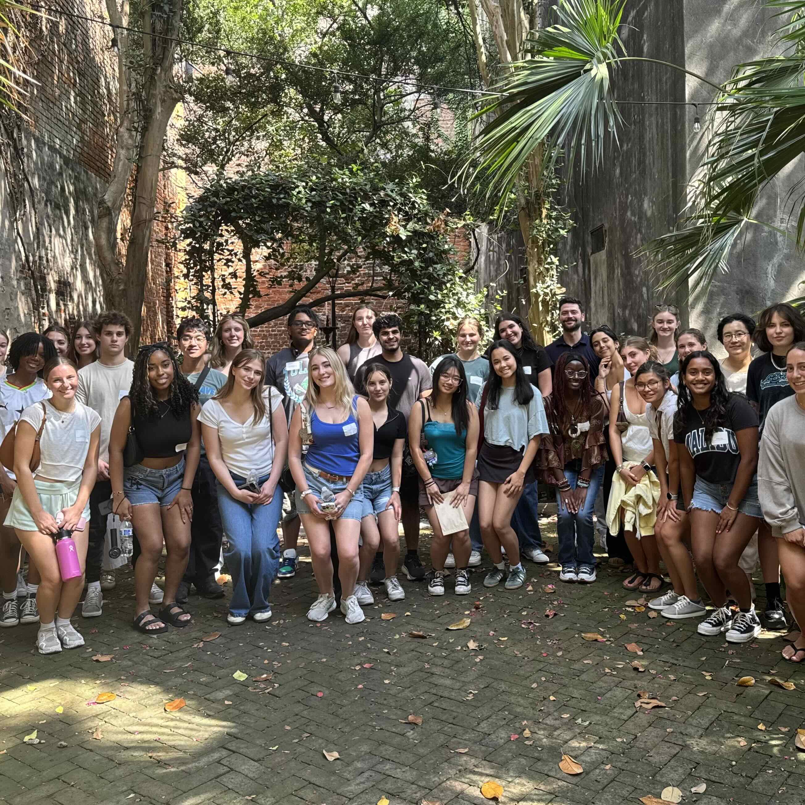 Photograph of a large group of smiling students in a leafy, brick-walled courtyard.