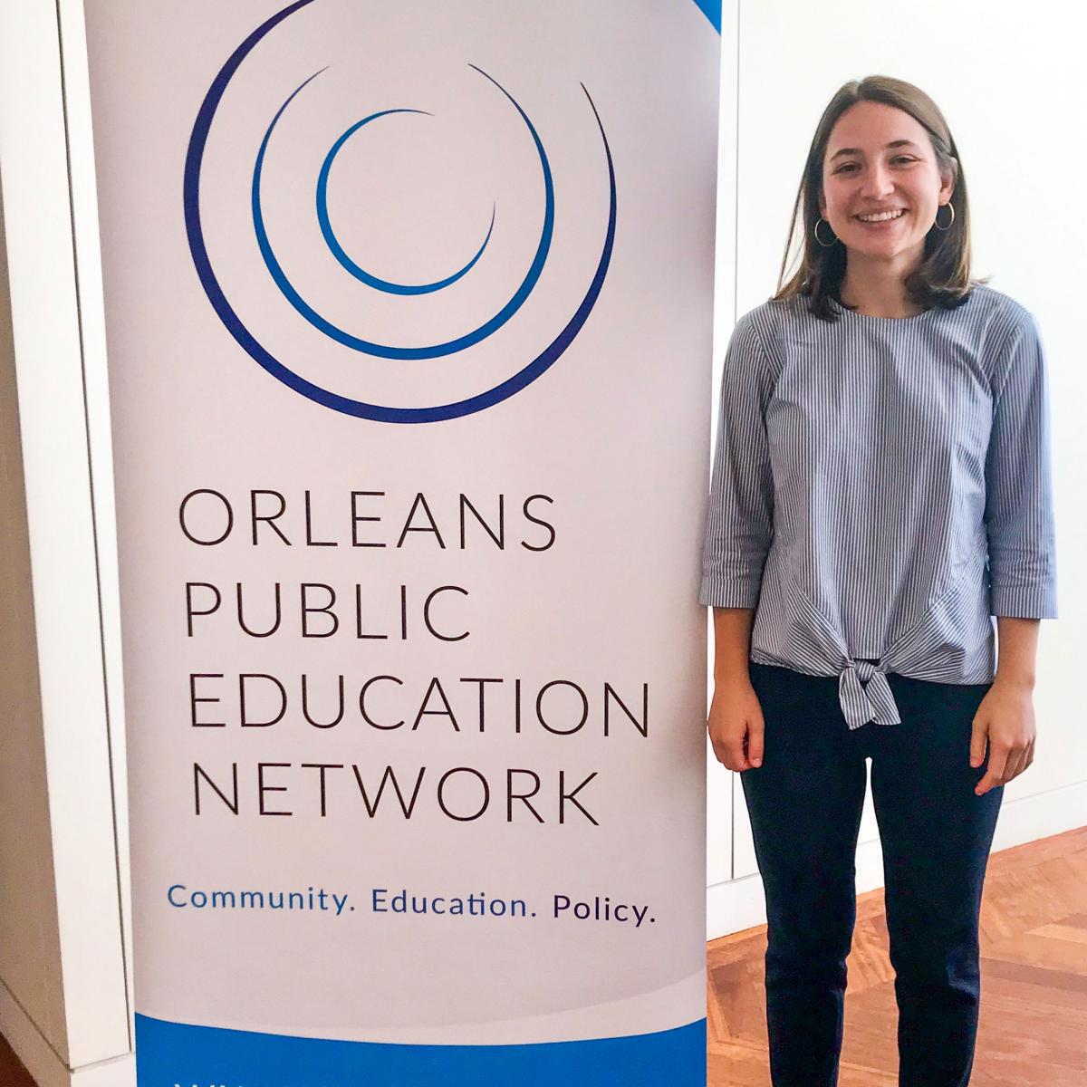 Student Standing Next to Orleans Public Education Network Banner