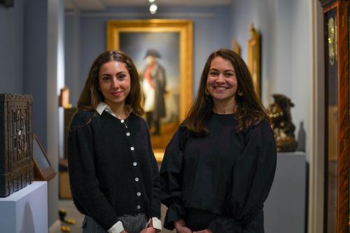 Naya Ben-Meir and Emily Otranto pose in a hall in M.S. Rau with a large portrait painting in the background.
